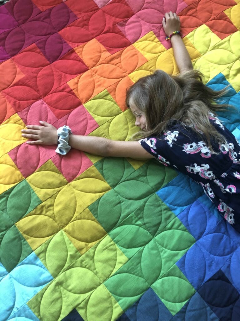 Image shows girl on rainbow quilt