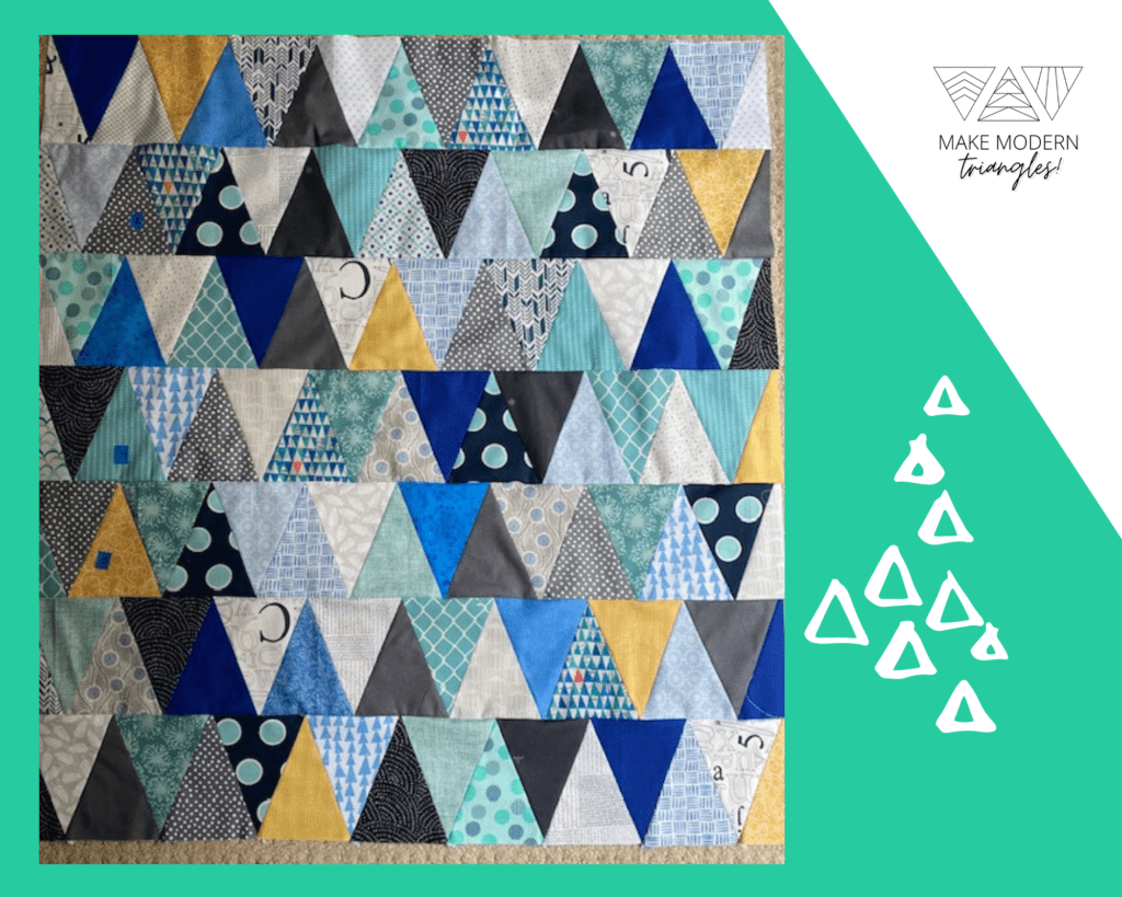 Modern triangle quilt made with print fabrics in blue, gray, black and yellow.