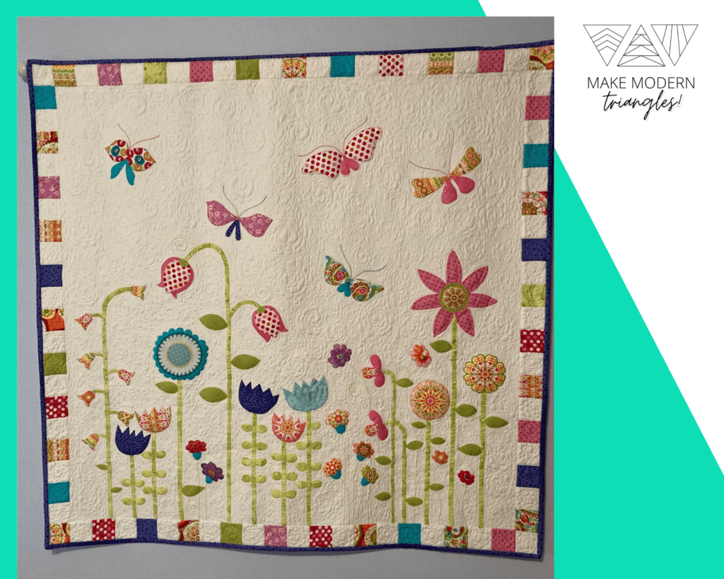 Appliqued quilt with flowers and butterflies iastel colors made by Lynn K., featured member in Make Modern Triangles.