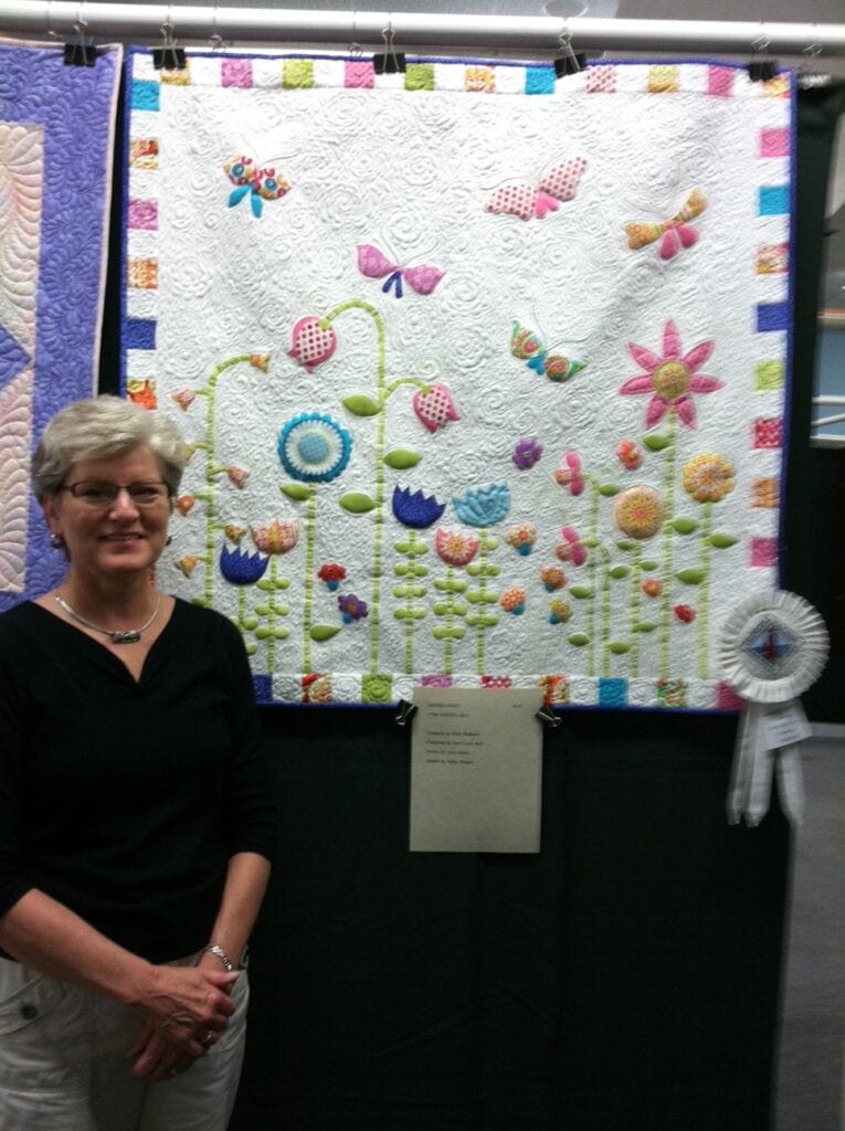 Lynn K, featured member spotlight, stands next to her winning quilt entry.