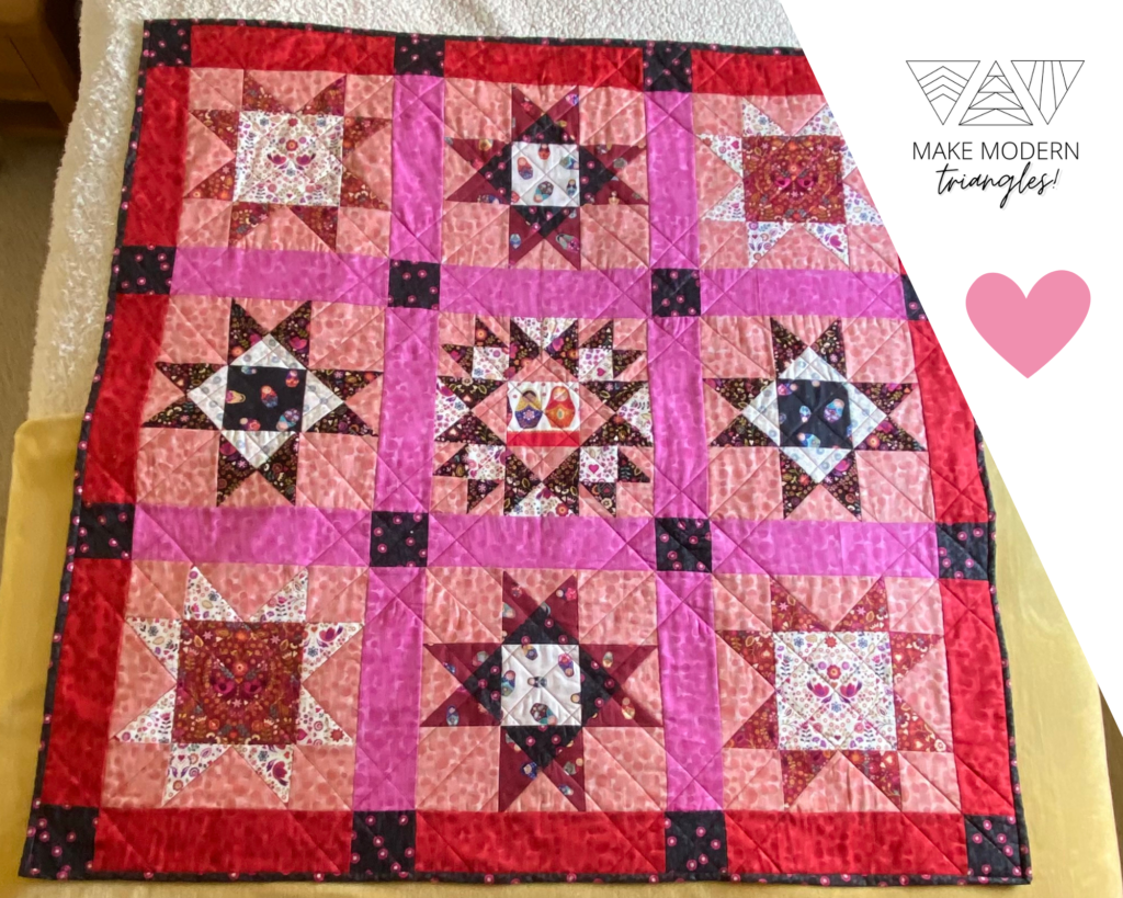 Star block quilt sampler made with red, pink and black print fabrics with Matryoshka motifs.