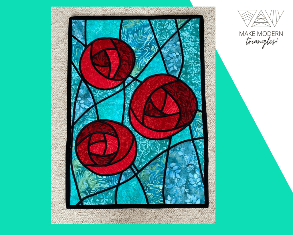 Stained glass fabric quilt featuring three red roses on a teal batik fabrics background.