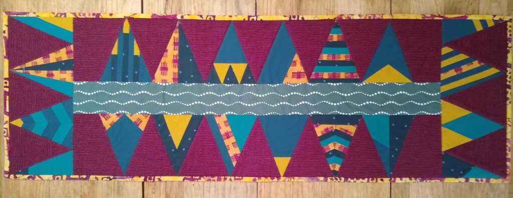 Member used an unusual color palette for the Merry Modern Triangles project in burgundy, dark teal, gold and navy fabrics.