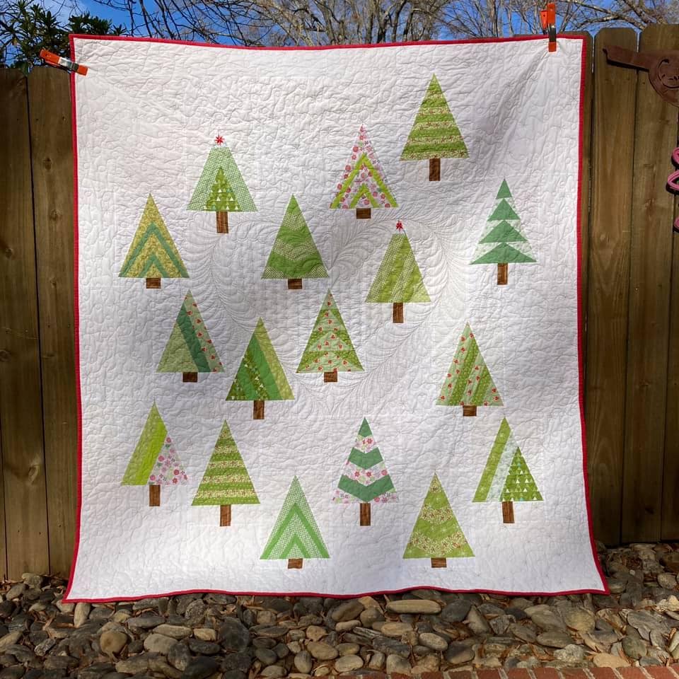 Member Susan T.s quilt with modern triangles tree blocks in various green fabrics depicting blocks included in the quilt along.