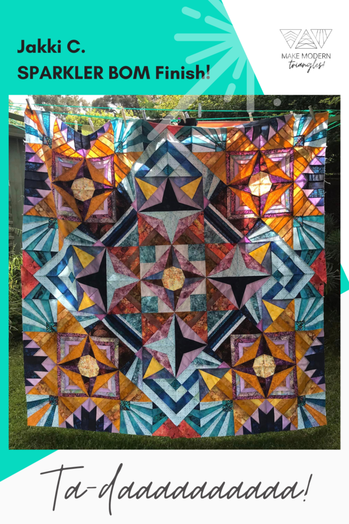 Sparkler quilt photo taken outdoors and resembles a stained glass window with light shining through the colored fabrics. 