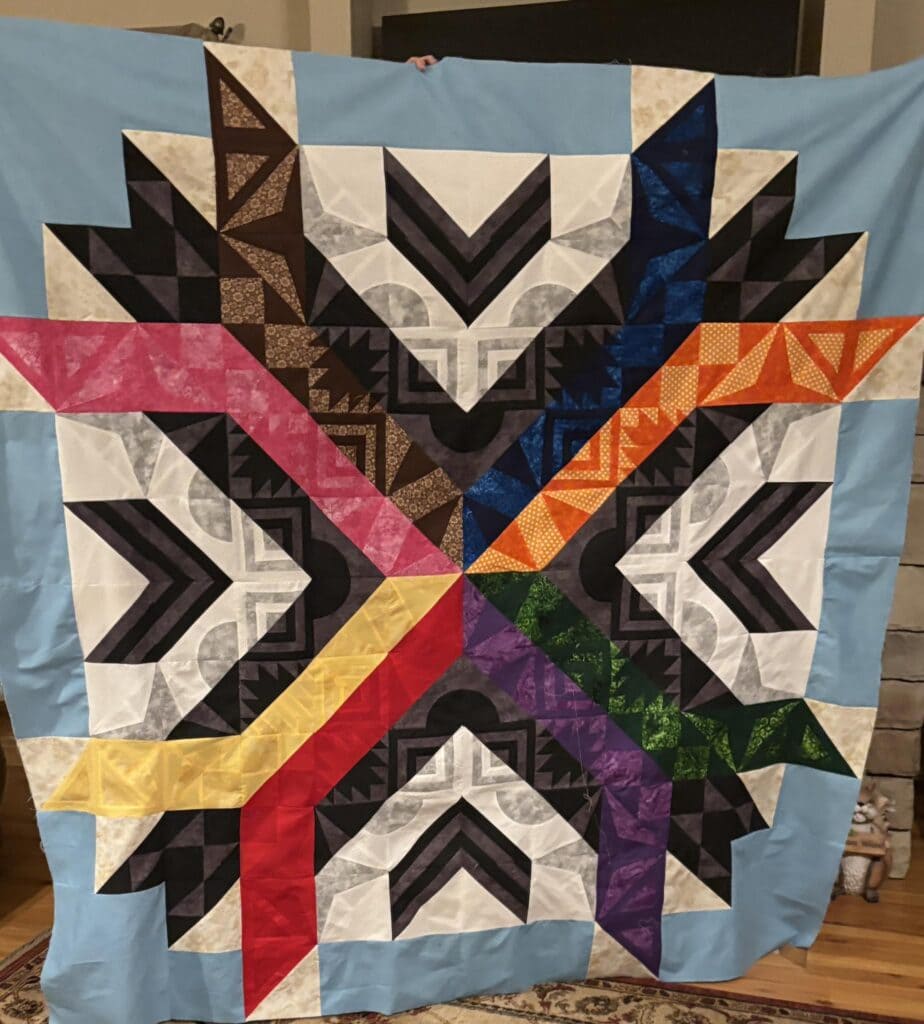 Progress on Aurora BOM quilt by Make Modern Triangles member Shirley R. Aurora rainbow color palette on white and gray background.