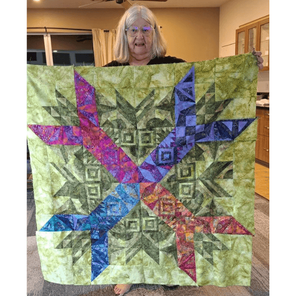 Aurora BOM quilt made with a green background and bright jewel tone modern triangles.