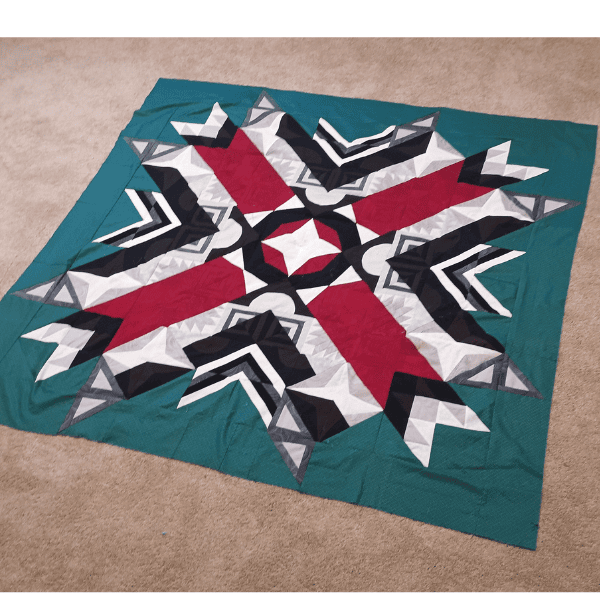 Aurora BOM quilt made with dark teal, red, gray and black fabrics.
